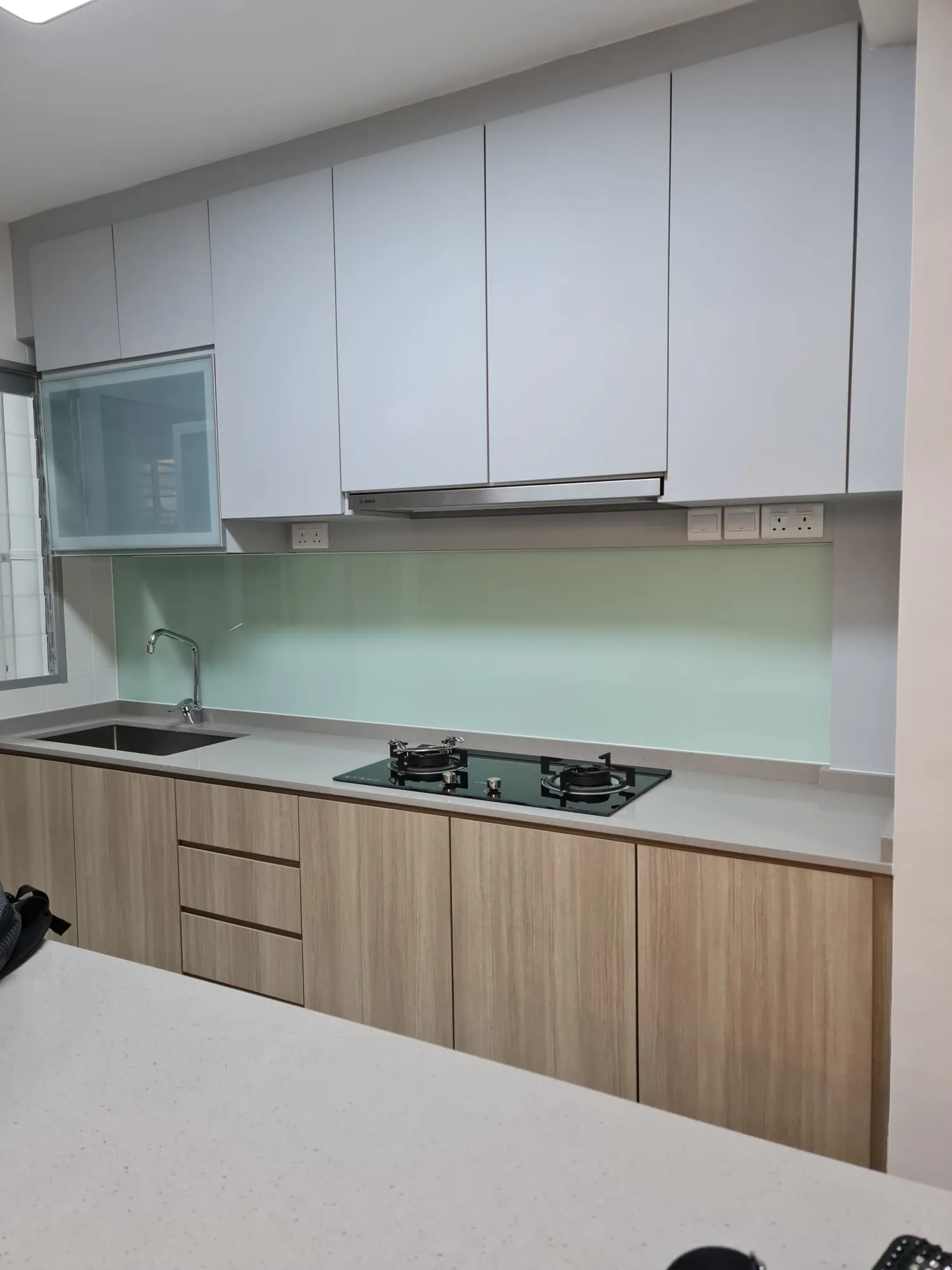Jurong HDB kitchen with white cabinetry, warm wood tones and a pale mint backsplash
