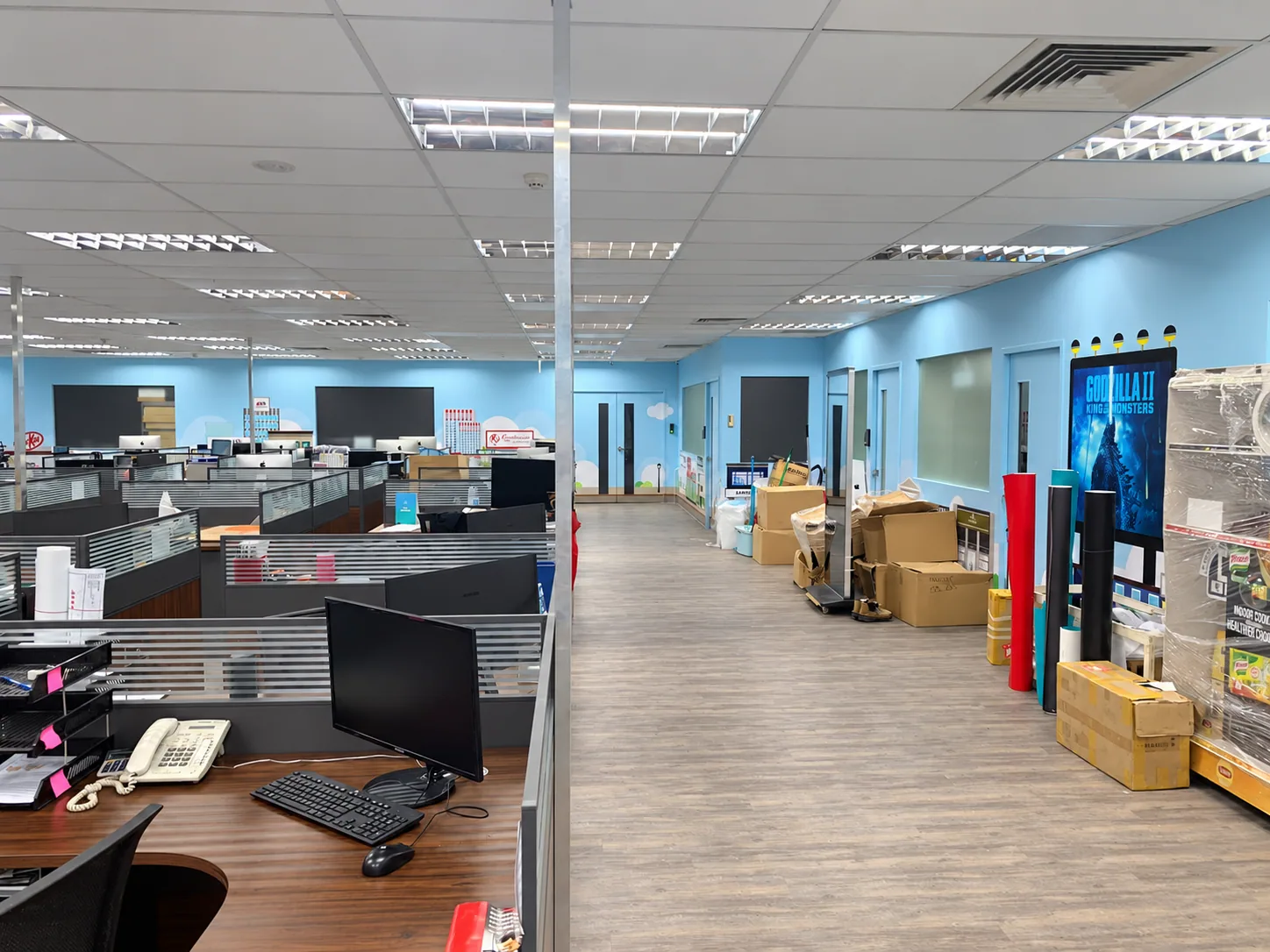 Printing-company office circulation aisle beside wood-toned workstations