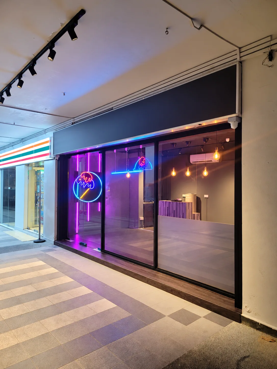 Anonymized Tampines ice cream shopfront with black-framed glazing and coloured lighting